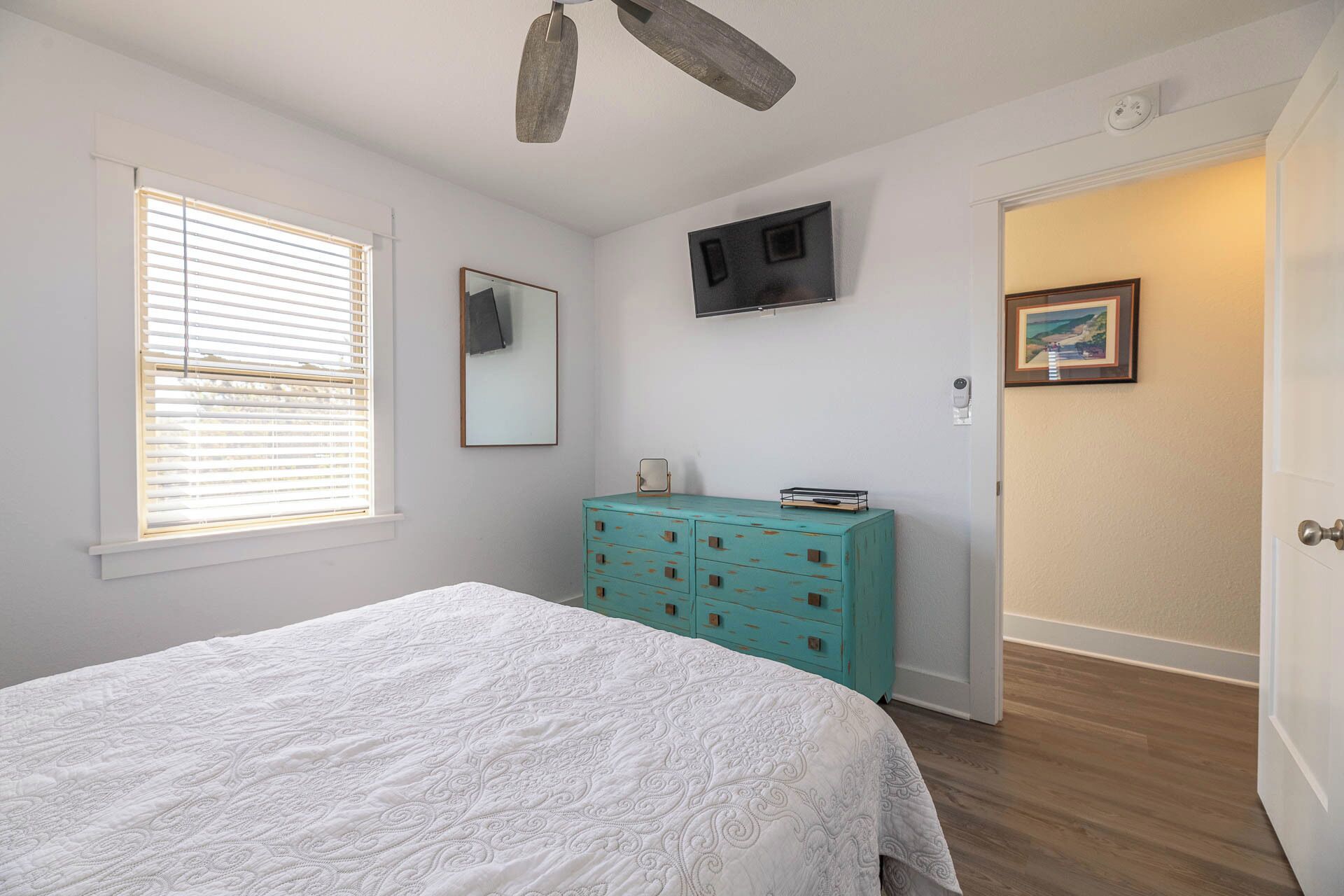 A bedroom with a bed, a dresser, a television, and a door leading to another room.