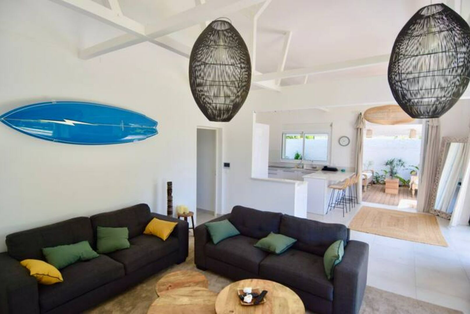 Una sala de estar moderna con dos sofás oscuros, una mesa de centro y una tabla de surf azul en la pared.