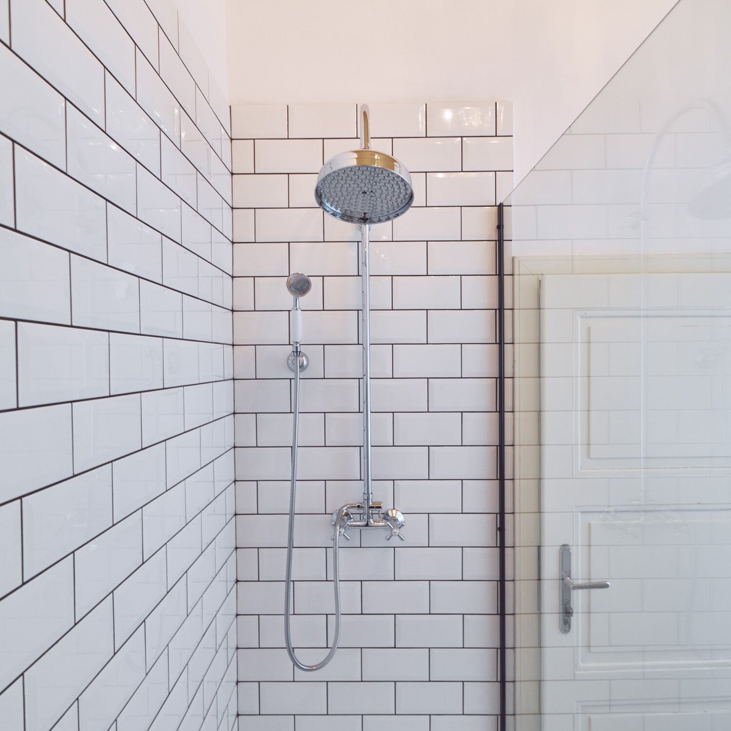 A shower area with white tiled walls and a glass door.