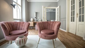 Um quarto com duas poltronas cor-de-rosa, uma mesa redonda com um vaso, e piso de madeira.