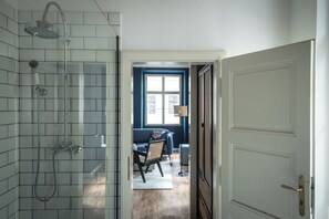 Un baño con ducha, una puerta blanca y vistas a una sala de estar con una pared azul y una ventana.