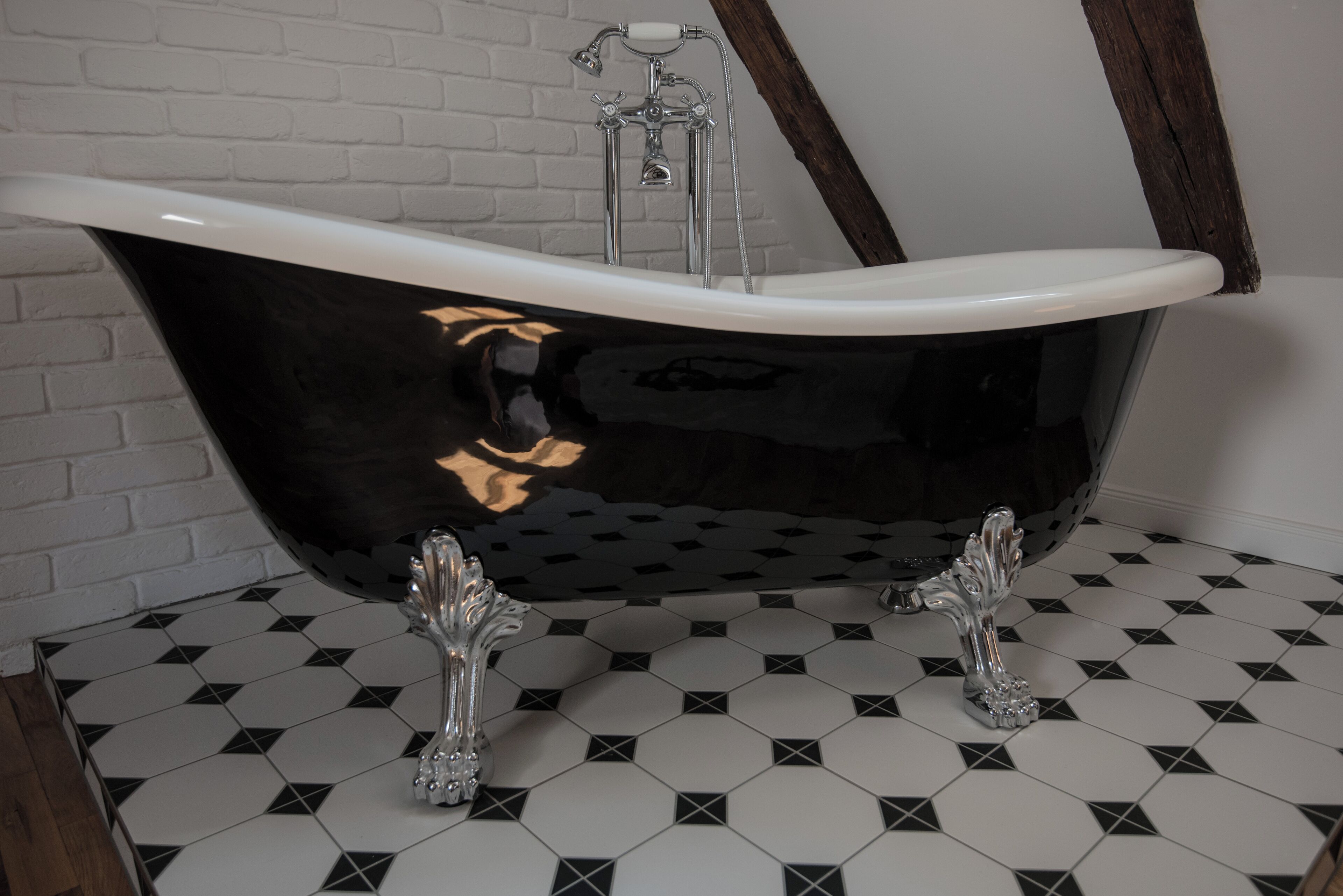 Une baignoire noire avec un intérieur blanc, des robinetteries chromées et un carrelage au motif géométrique.