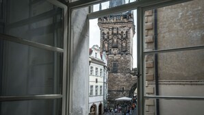 Janela aberta com vista para uma torre histórica e uma rua movimentada lá embaixo.