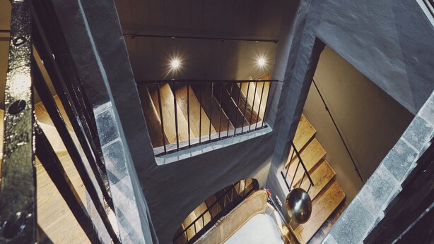 Um interior com vários níveis, uma escadaria, um banco de madeira e um objeto esférico no nível inferior.