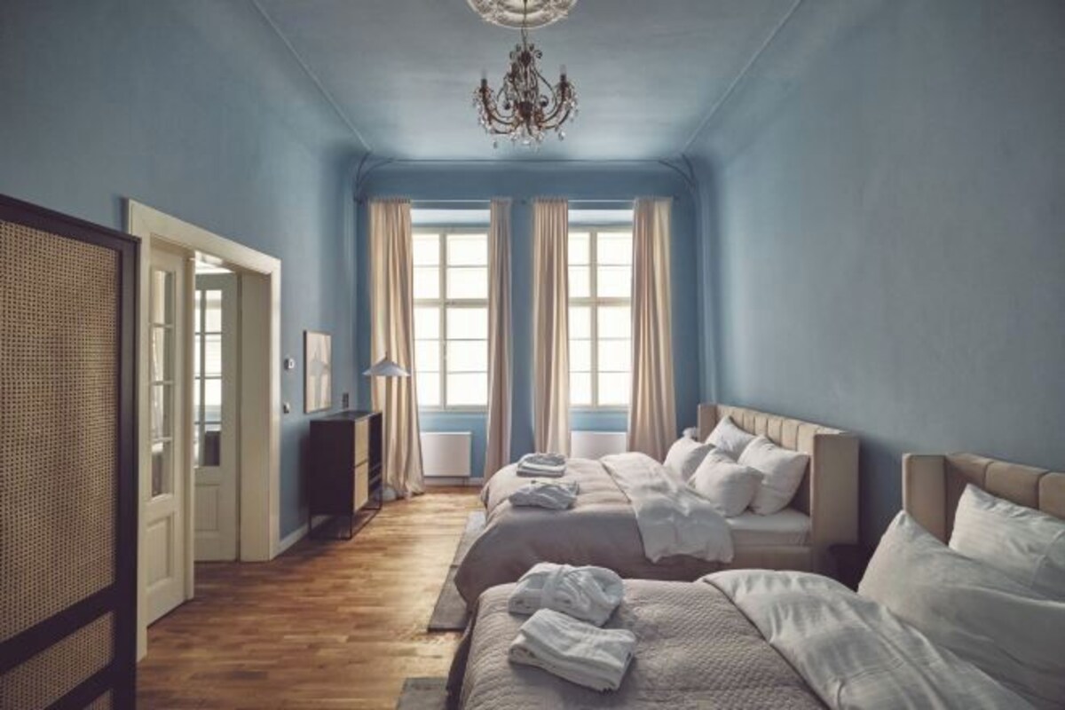 Ein Schlafzimmer mit zwei Betten, einer Chandelüster und großen Fenstern mit Vorhängen.