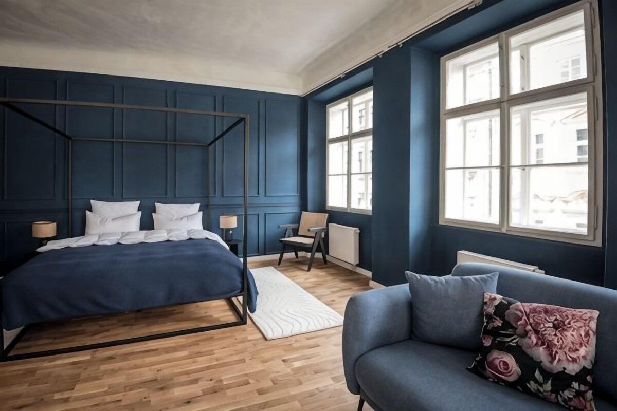 Ein Schlafzimmer mit einem Bett, einem Sessel, einer Couch und großen Fenstern.