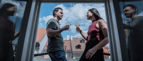 Un couple trinque avec des verres de vin dans une pièce d’où l’on peut admirer des bâtiments et un ciel dégagé.