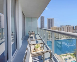 A balcony with a glass railing, a table with chairs, and a view of a cityscape with high-rise buildings.