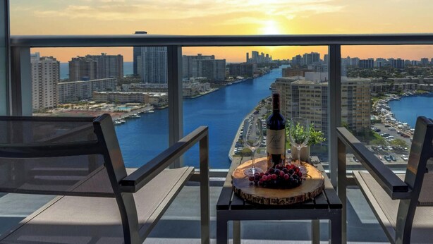 A balcony with a city view, a bottle of wine, and a fruit platter. - Infinite View 1BR w/ Balcony & Pool (Hallandale Beach)