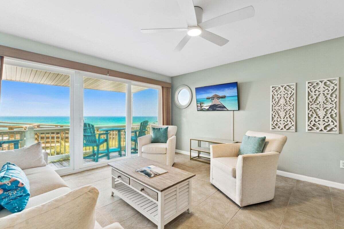 Een ruime woonkamer met uitzicht op zee, een plafondventilator en een schilderij aan de muur.
