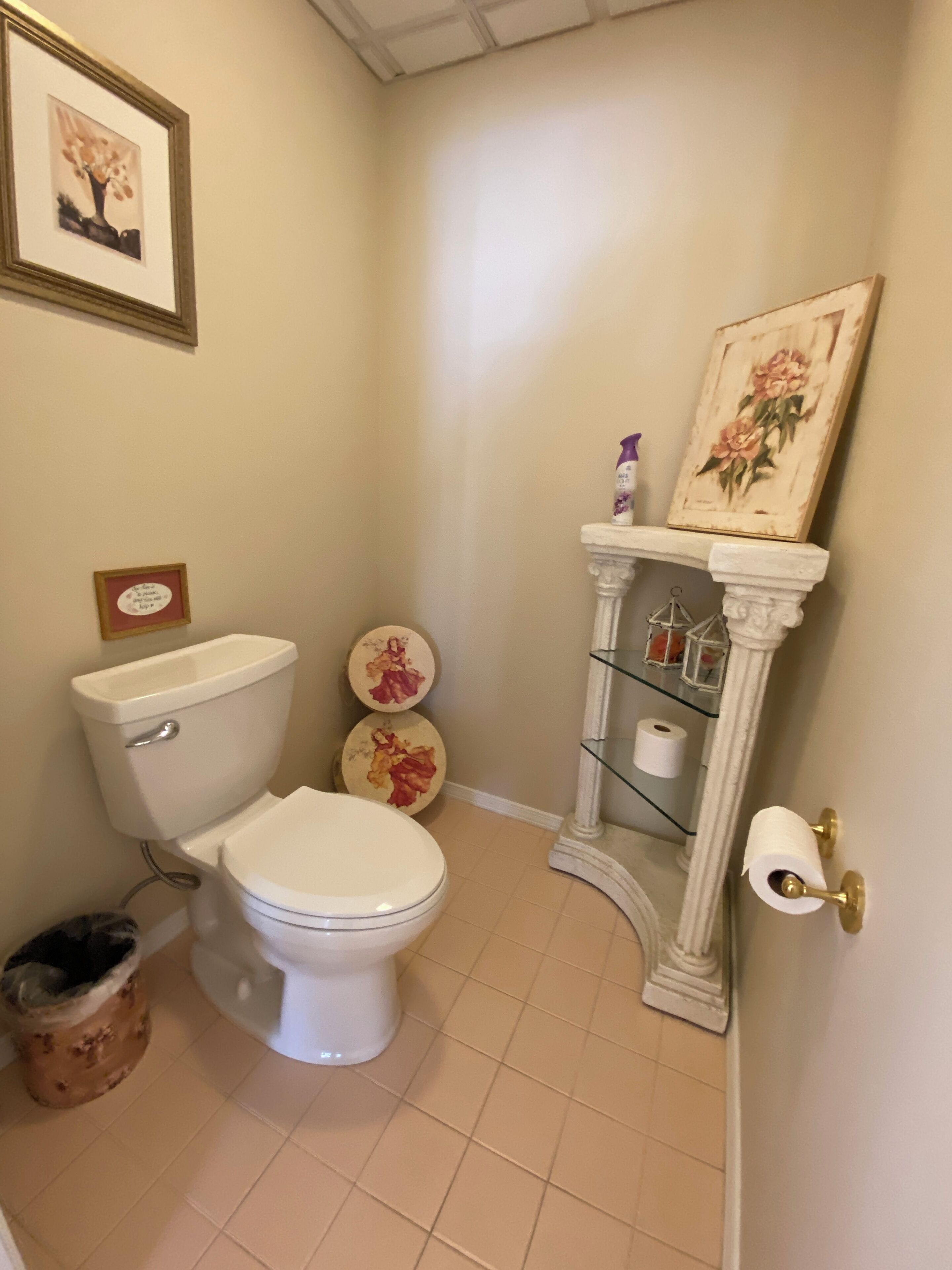 A bathroom with a toilet, two decorative plates, a toilet paper holder, and a trash bin.
