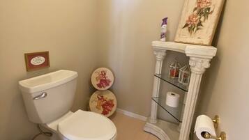 A bathroom with a toilet, two decorative plates, a toilet paper holder, and a trash bin.