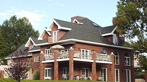 A large brick house with multiple balconies, a well-maintained lawn, and a clear sky. - Toad Hall Manor  (Butte)