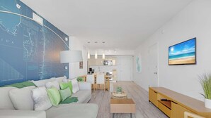 A modern living room with a large map on the wall, a dining area, and a kitchen in the background. - Infinite View| Balcony| Pool+ Gym (Hallandale Beach)