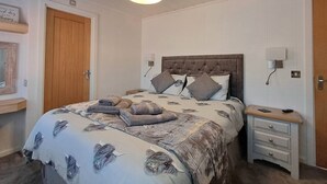 Un dormitorio con cama, mesitas de noche, lámpara y puerta.