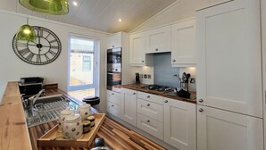 Una cocina moderna con armarios blancos, encimera de madera y una lámpara colgante verde.