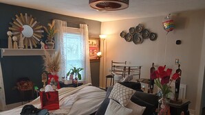 Un dormitorio con cama, un sofá gris, una mesita redonda y una ventana con cortinas.
