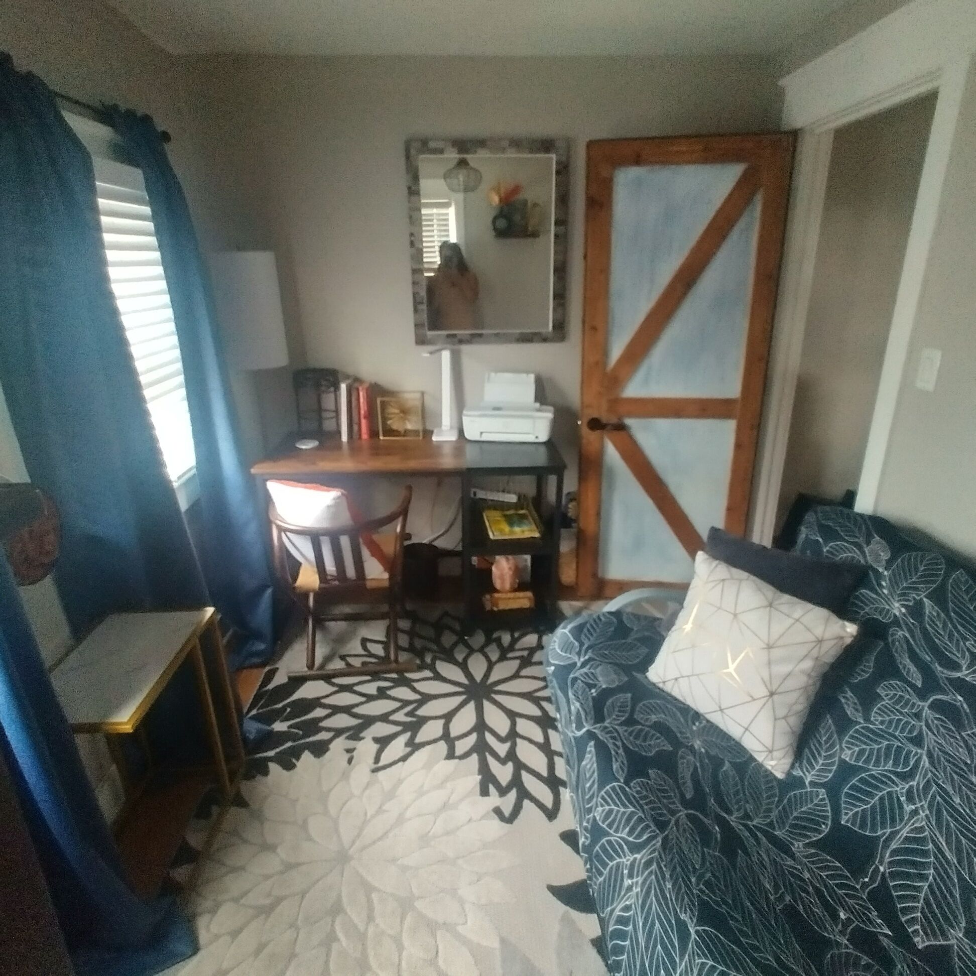 Ein kleiner Wohnraum mit Schreibtisch, Stuhl und einem gemusterten Sofa.