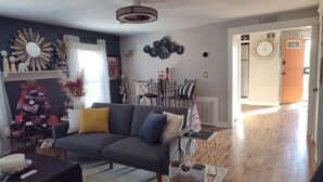 Una sala de estar con un sofá gris, una pared decorativa y un comedor con sillas y una mesa.