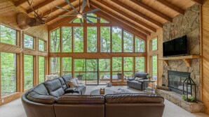 A spacious living room with a large leather sectional sofa, a stone fireplace, and a television mounted on a stone wall. - Alpine Woods by Innsbrook Vacations! (Innsbrook)