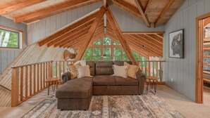 A loft-style room with a sloped ceiling, a large window, a brown sectional sofa, and a patterned rug. - Alpine Woods by Innsbrook Vacations! (Innsbrook)
