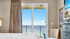 A hotel room with a bed, a chair, a dresser, and a balcony with a view of the ocean.
