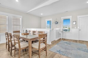 Un comedor con una mesa y sillas de madera, vista al exterior a través de una ventana, y una escalera que sube a otro nivel.