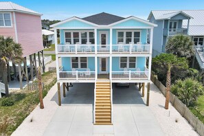 Una casa de varios pisos frente a la playa, con una escalera central, balcones y una zona de arena.