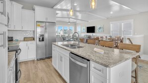 A modern kitchen with white cabinetry, a granite countertop, stainless steel appliances, and pendant lighting. - Vitamin Sea: Coastal Chic Home with Private Pool, Elevator (Oak Island)