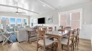 A spacious living room with a dining area, wooden flooring, and a ceiling fan. - Vitamin Sea: Coastal Chic Home with Private Pool, Elevator (Oak Island)