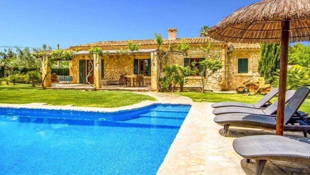 A poolside area with lounge chairs, a stone building with a tiled roof, and a thatched umbrella. - Villa Roig, Stone villa in the country (Pollença)