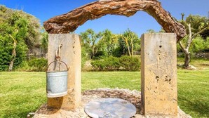 A rustic outdoor structure with a metal bucket hanging from a wooden beam, surrounded by greenery. - Villa Roig, Stone villa in the country (Pollença)