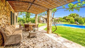 An outdoor patio area with stone flooring, wicker furniture, and a pool in the background. - Villa Roig, Stone villa in the country (Pollença)