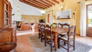 A rustic dining area with a wooden table and chairs, a stone fireplace, and a cozy living room with sofas and a TV. - Villa Roig, Stone villa in the country (Pollença)