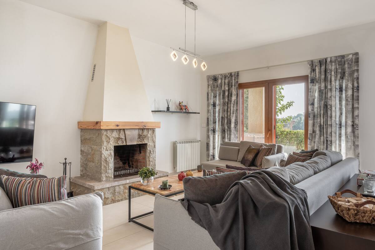 A modern living room with a stone fireplace, a large window with curtains, a sofa, and a television.