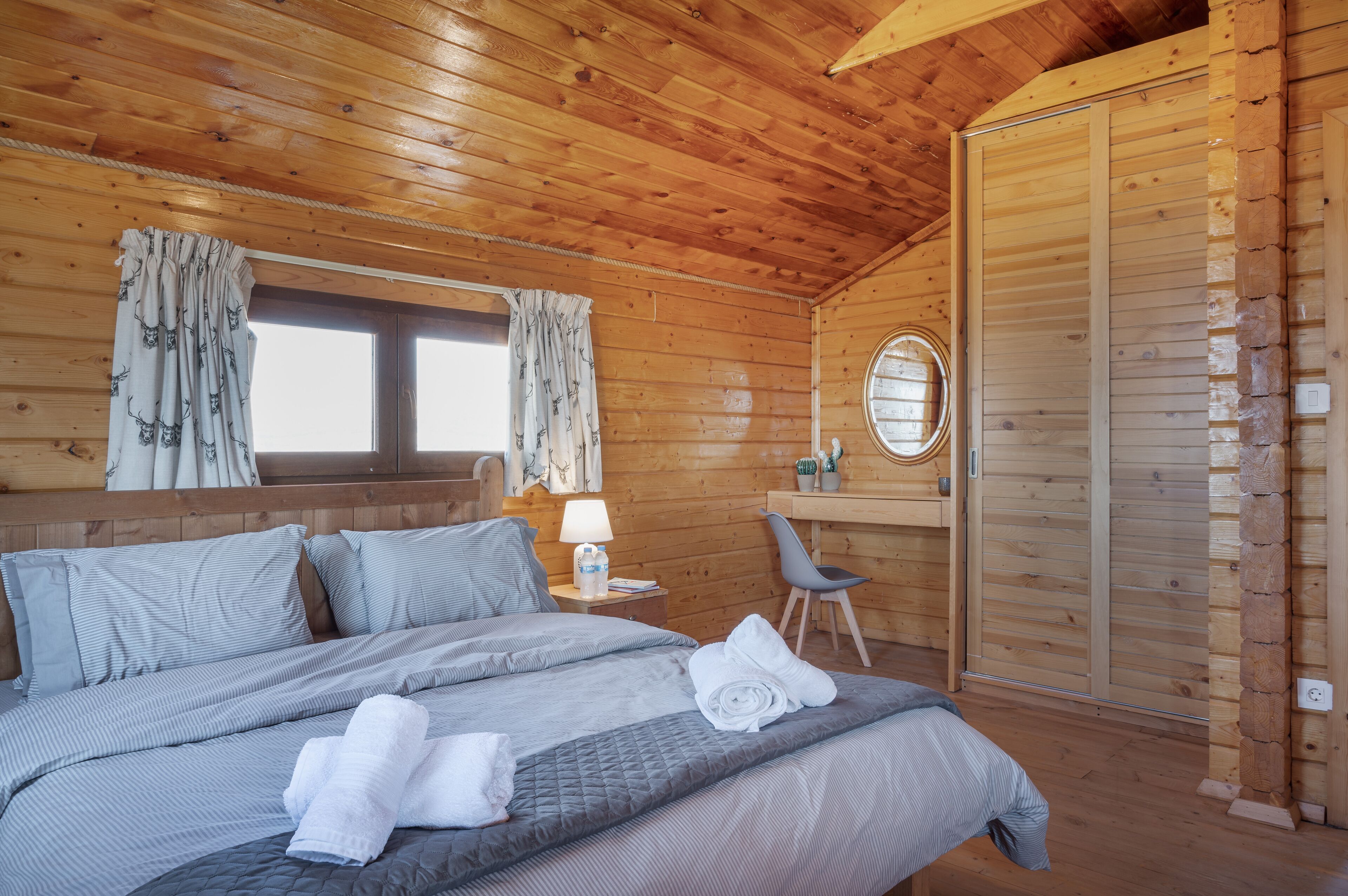 A wooden cabin room with a bed, a desk, and a chair.