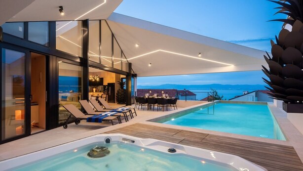 Et moderne udendørs poolområde med jacuzzi, liggestole og et spisebord.