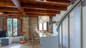 Een moderne keuken met een centraal eiland, houten balken in het plafond en een uitzicht op de omgeving door grote ramen.