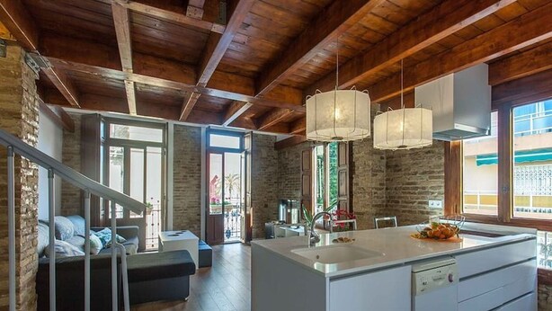 Een moderne keuken met een centraal kookeiland, een eethoek met een bank, en een trap die naar een ander niveau leidt.