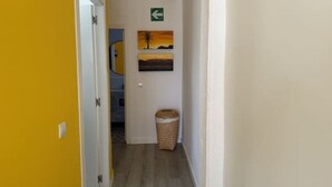 Un couloir avec un mur jaune, une porte blanche, un panneau de signalisation vert et un tableau représentant un coucher de soleil.