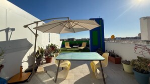 Une terrasse sur le toit, avec une table et des chaises, des plantes en pot et un grand parasol.