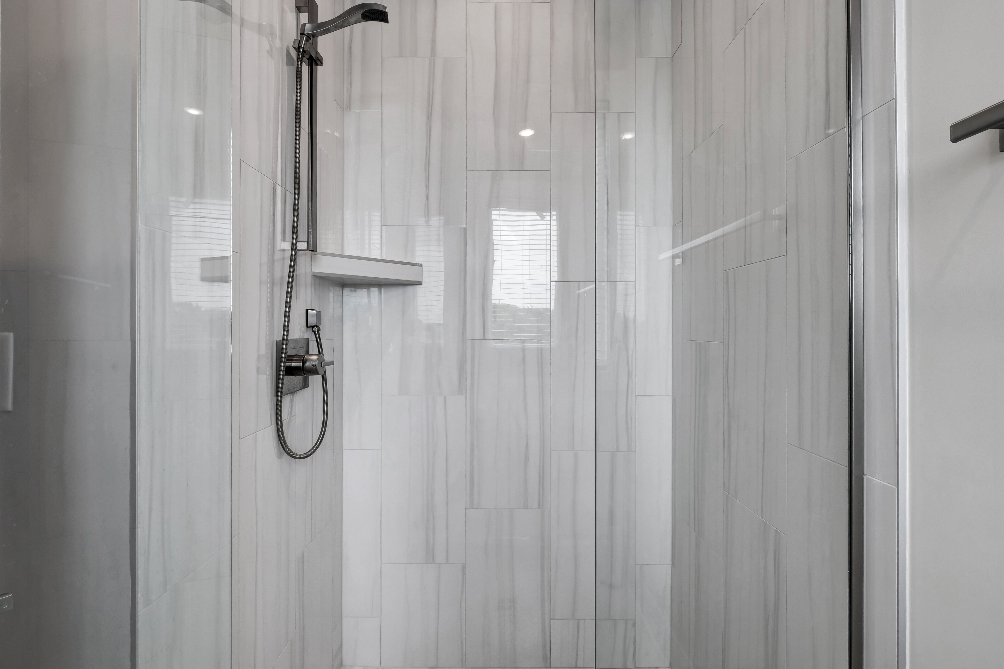 A modern shower with a handheld showerhead and a wall-mounted control panel.