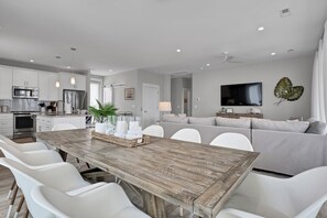 A modern kitchen with white cabinets, stainless steel appliances, and a dining area with a wooden table and white chairs.