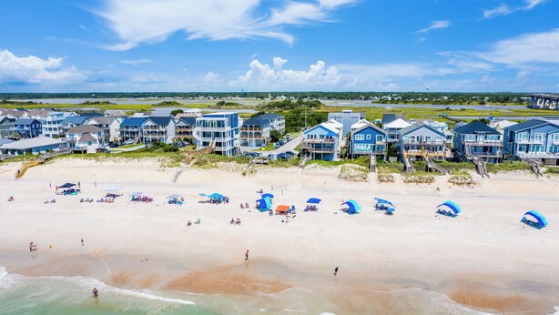 Ein Strandhotel mit mehrstöckigen Gebäuden, einem Sandstrand und Sonnenschirmen.