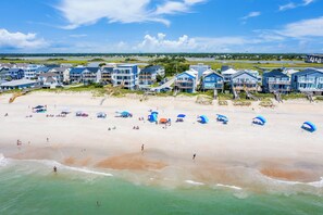 A beachfront hotel with multiple-story buildings, a sandy beach, and umbrellas. - Eagle's Nest #140- Coastal Modern Luxury in the Heart of Surf City, NC (Surf City)
