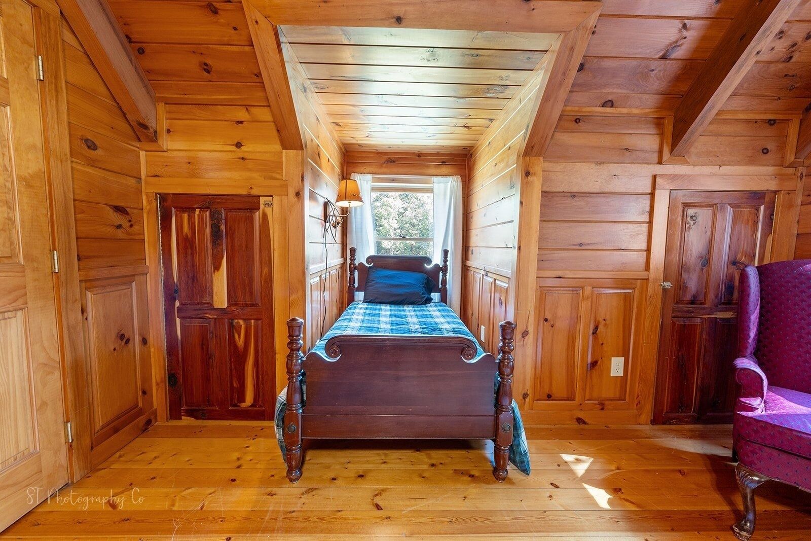 Habitació d'una cabana de fusta amb un llit, una cadira i una finestra.