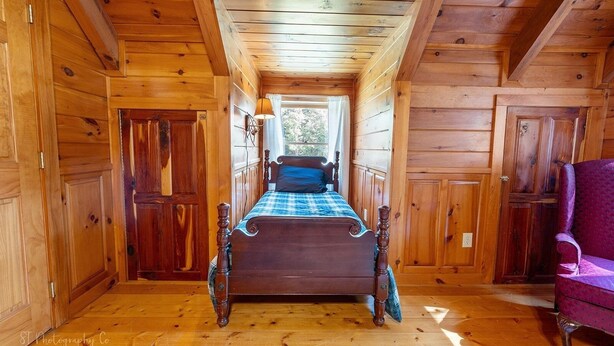 A wooden cabin room with a bed, a chair, and a window. - Burning Tree 3 Bedroom Cabin by RedAwning (Sevierville)