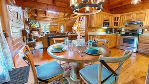 A wooden cabin interior with a dining area, kitchen, and a staircase leading to a loft.