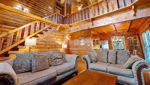 A log cabin interior with a staircase, two sofas, a coffee table, and a chandelier.
