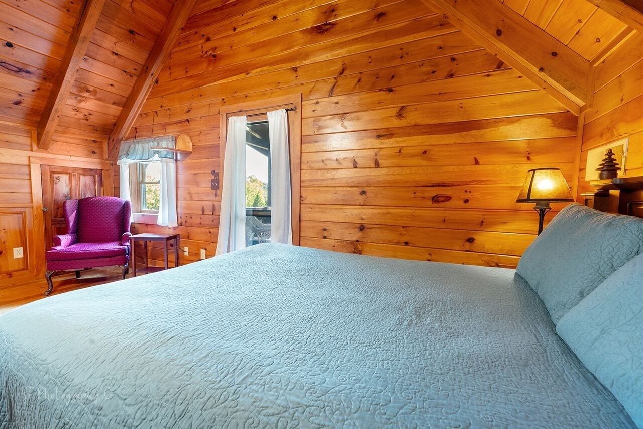 Una habitación de cabaña de madera con una cama, una silla, una mesa y una ventana.